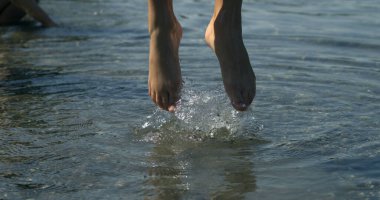 Çocuk bacakları süper yavaş çekimde zıplıyor. Su dalgaları ile 800 fps, küçük bir kız yukarı sıçrıyor. Yakalandı, doğayla temas kuruldu.