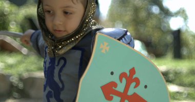 Geleneksel ortaçağ kostümü giymiş küçük bir çocuk kılıçla vuruyor ve kalkanı tutuyor, hız rampası.