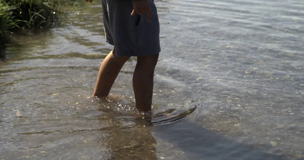 Child legs and feet entering lake water by shore enjoying nature, captured