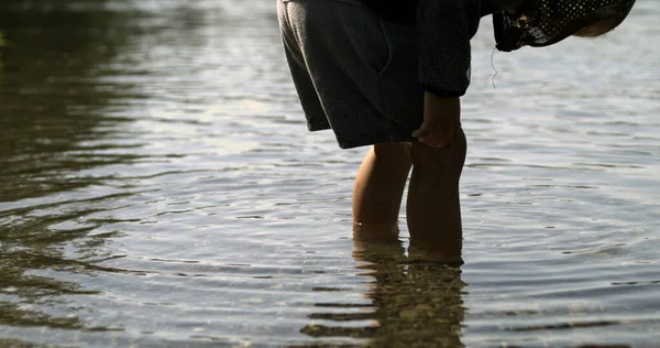 Child legs standing in lake water with ripples flowing in super slow-motion, captured