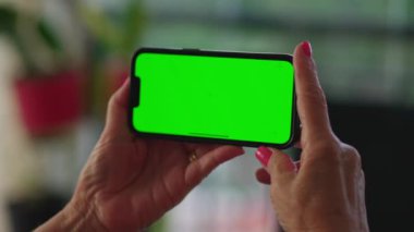 Krom yeşil ekranlı akıllı telefon cihazını yatay olarak tutan eller. Çevrimiçi içeriğe bakan yaşlı insan eli