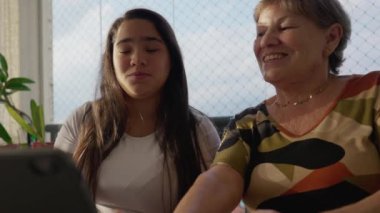 20 'li yaşlarda yetişkin bir kız 70' li yaşlarda yaşlı bir kadına tabletle yardım ediyor.