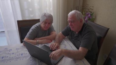 Evde dizüstü bilgisayar kullanan yaşlı bir çift. Yaşlılık ve modern teknoloji. Online içeriği gösteren bilgisayar ekranına bakan yaşlılar
