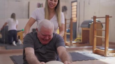 Yaşlı Adam, Kadın Koçun Fizyoterapi Rehberi altında Pilates Topuyla Esniyor, Yaşlılık Egzersizleri Rutini