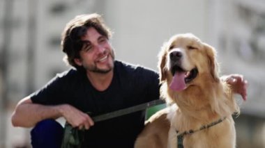 Güneşli bir günde parkta Golden Retriever köpeğiyle poz veren genç bir adam. Hafta sonu köpek eşliğinde eğlenen kişi