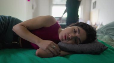 Bunalımda olan bir çift: üzgün bir ifadeyle yatakta yatan depresyondaki genç kadın kızgın erkek arkadaşın çığlıklarını ve arka planda vücut hareketlerini dinliyor.