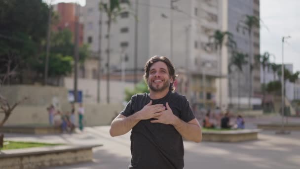 一个有希望的年轻人把手放在胸前 感到感激和幸福 一个快乐的男性高加索人 30多岁 兴高采烈地站在城市里 — 图库视频影像