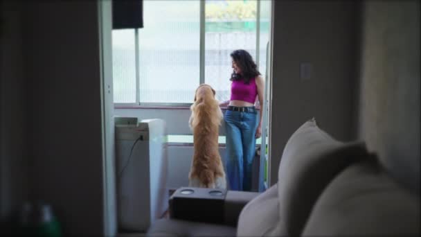可爱的年轻女人 她的狗站在公寓里靠窗站着 30多岁的成年女孩在她的金发女郎旁边 真实的家庭生活方式 — 图库视频影像