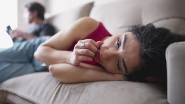 彼女のボーイフレンドが背景の電話で見つめている間 疲労感のある表情でソファの上に寝そべっている女性を優先 精神的苦痛を持つ女性 — ストック動画