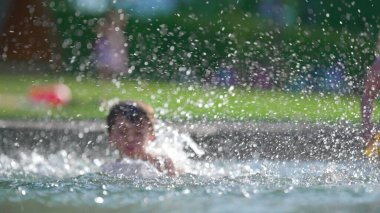 Havuzda her yere su sıçrayan bir çocuk.