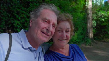 Parktaki bankta güneşli günün tadını çıkaran neşeli yaşlı çift. Koca yaşlı karısına sarıldı. Gülümsüyor ve dışarıda gülüyor. Mutlu bir evlilik.
