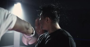 Dövüş Dövüşçüsü, 800 fps ağır çekimde boks ringinde yumruk yiyor. Yakın plan erkek yüzü havada uçuşan ter damlacıklarıyla vuruluyor