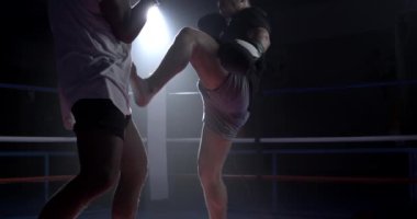 Muay Thai dövüşçüsü boks ringinde bacağıyla vuruyor yavaş çekimde 800 fp hız rampası ve dramatik spot ışığı ile