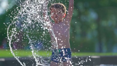 Coşkulu bir çocuk yaz öğleden sonra havuzda gökyüzüne su püskürtüyor. Küçük bir çocuk yüzme havuzuyla 120fps 'de havaya su sıçratıyordu.