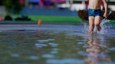 Yüzme havuzunda koşan neşeli çocuk yaz günü yavaş çekimde su sıçratıyor. Hızlı koşan aktif küçük çocuk.
