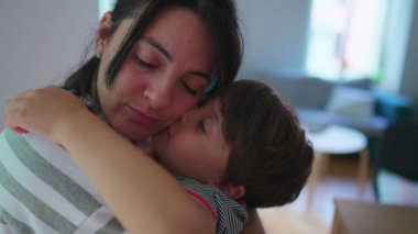 Anne küçük oğlunu şefkatle kucaklıyor. Sevecen bir anneye sarılmış kolları ve yanakları gerçek aşkla çevrili bir çocuk.