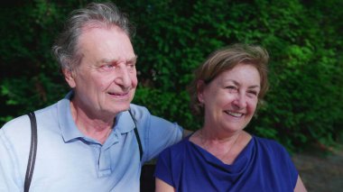 Yaz günü kameraya poz verirken sırıtan ve gülen yaşlı bir çift arasında komik bir an var.