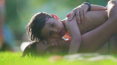 Küçük oğlunun yaz tatili sırasında çimlerin üzerinde yatarken annesini yanağından öptüğü sevgi dolu bir an. Aile hayatı, sevgi ve özeni betimler, ten tene