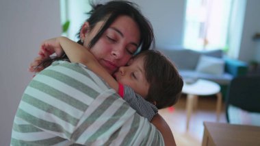 Anne küçük oğlunu şefkatle kucaklıyor. Sevecen bir anneye sarılmış kolları ve yanakları gerçek aşkla çevrili bir çocuk.