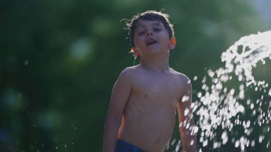 Belediye havuzunda havuz başında havuz başında güneşlenen küçük bir çocuk. Yüzme yerindeki fıskiyelerden gelen şen şakrak sulardan zevk alan çocuk.