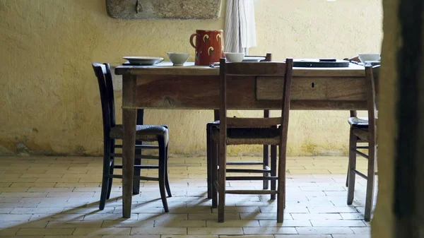 Rural indoors of wooden rustic table and chairs on display for lunch or supper. Traditional antique farmhouse interior with plates and water vase in simple and humble living