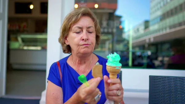 Senior Lady Relishing a Cold Ice-Cream Treat on a Sunny Day at Parlor Shop. Older woman savoring waffle cone dessert