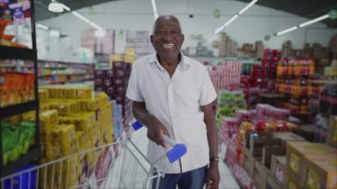 Alışveriş arabasında gülümseyen ve süpermarkette kameraya bakan Afrikalı Amerikalı son sınıf öğrencisinin portresi.