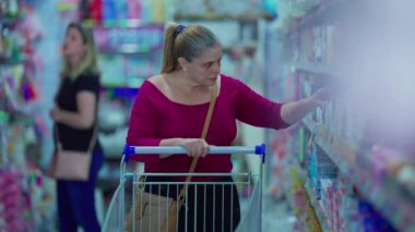 Alışveriş arabalı bir kadın süpermarketten mal seçiyor.