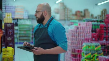 Market koridorundaki tablet cihazıyla envanteri kontrol eden erkek çalışanlar raflara bakan ve süpermarketteki ürünleri incelemek için modern teknolojiyi kullanan personel.