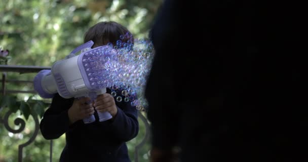 Маленький Мальчик Распыляет Тысячи Мыльных Пузырей Большим Игрушечным Пистолетом Супер — стоковое видео