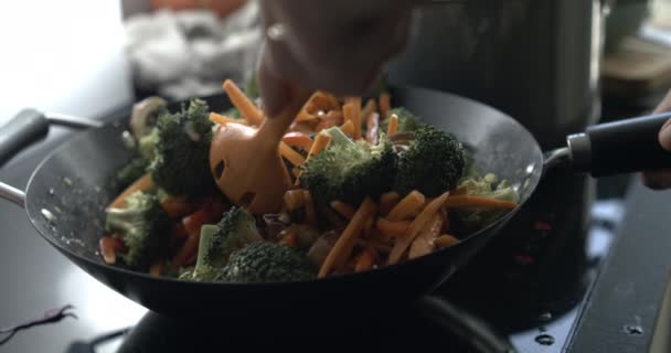 キッチンストーブで熱い鍋で野菜をかき混ぜるクローズアップ ブロッコリーとニンジン — ストック動画