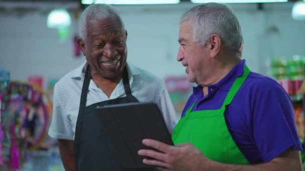 タブレットPcとユニフォームでカメラで笑顔のスーパーマーケットチェーンの多彩なブラジルのシニアスタッフ アフリカ系アメリカ人の高齢者と白人男性が一緒に笑う — ストック動画