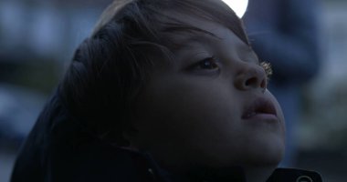 Düşünceli düşünceli çocuğun yakın plan yüzü öğleden sonra alacakaranlıkta boş bir ifadeyle yukarı bakıyor.