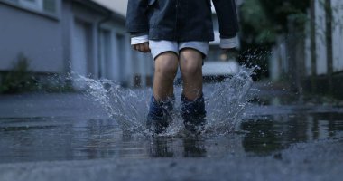 Çocuk havada zıplıyor ve su birikintisine sıçrıyor. 800 fps hızla çekiliyor. Yağmurdan sonra neşeli bir eğlence.