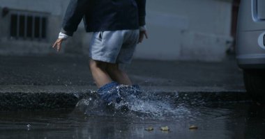 Çocuğun her yere su sıçratması caddede su birikintisine düşmesi yüksek hızlı kamerayla 800 fps yağmur botu giymesi.