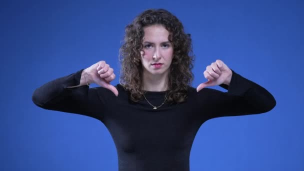 女人放下大拇指拒绝提供 20多岁的女性不喜欢被拒绝 看着蓝色背景的相机 — 图库视频影像