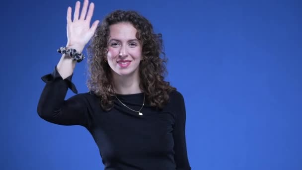 Szczęśliwa Kobieta Witająca Kamerę Gestem Ręki Stojącej Niebieskim Tle 20S — Wideo stockowe
