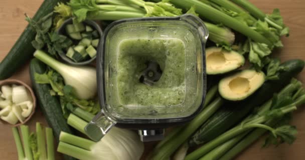 スローモーションでキャプチャされたブレンダー内の緑の野菜を混合するブレンダーのオーバーヘッドビュー セロリ アボカド フェンネル キュウリ フェンネルを背景としたデトックスジュースの調製 — ストック動画