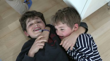 Kardeşler yerde yatıp güreşiyor. Kardeşler kavgası, aile rekabeti.