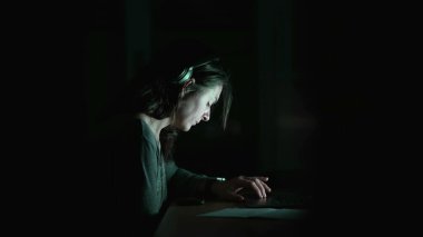 Gecenin bir yarısı zifiri karanlıkta dizüstü bilgisayarın önündeki kadın. Çevrimiçi internet okuma içeriğini tarayan samimi kişi