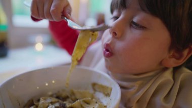 Yakasına peçete sıkıştırılmış küçük bir çocuk, restoranda spagettinin tadını çıkarıyor. Çocuk makarna yiyor.