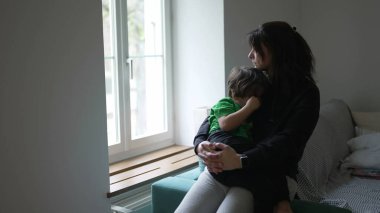 Anne yaralı çocuğu evde pencerenin önünde teselli ediyor. İçten, düşünceli, düşünceli bir annenin, küçük çocuğu teselli ettiği bir an.