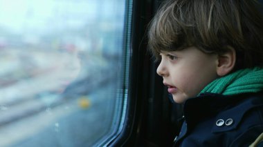 Trian penceresinden geçen manzaraya bakan küçük bir çocuk. Sonbahar sezonu seyahati sırasında atkı ve ceket giyen çocuk.