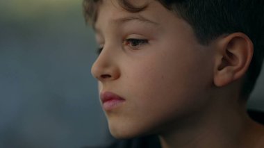 Düşünceli, içe dönük, yakından bakan, trenle seyahat eden bir çocuk pencereye bakıyor ve derin düşüncelere dalmış bir duyguyla yanından geçen manzaraya bakıyor.