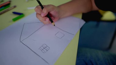 Yakın plan çocuk eli, geleneksel bir ev, iki pencere ve kağıt üzerinde kurşun kalemle ön kapı çiziyor, yaratıcılık oyun zamanı çocukluk kavramı