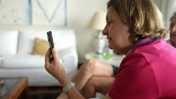 Grandmother holding smartphone device speaking with relatives with video call communication at home