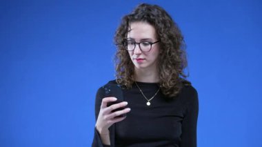 Mavi arka planda cep telefonu cihazını tutan bir kadın, mesaj bildirimini hoş karşılamıyor. Gözlük takan kişi beklenmedik haberlere tepki veriyor.