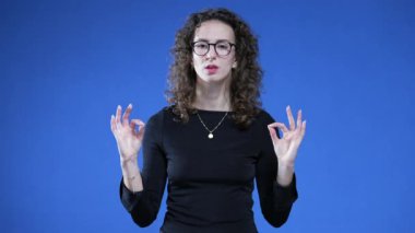 Elleri mavi arka planda dikilirken, kadın meditasyon yapıyor gözleri kapalı, derin bir nefes alıyor stresi atıyor.