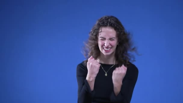 Mujer Salta Celebra Victoria Con Los Puños Pie Fondo Azul — Vídeo de stock