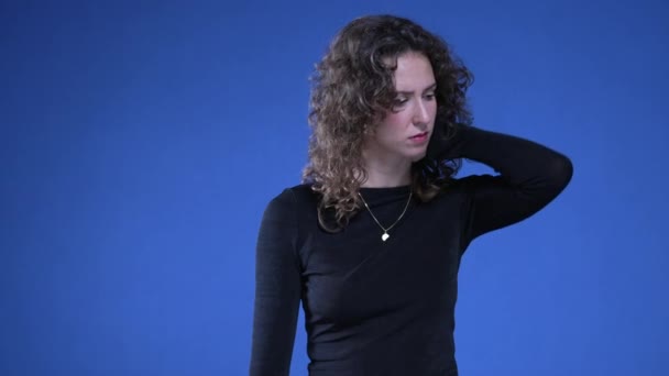 穿着紧绷的年轻女子一边摸着脖子 一边站在蓝色的背景上试图减轻精神上的痛苦 — 图库视频影像